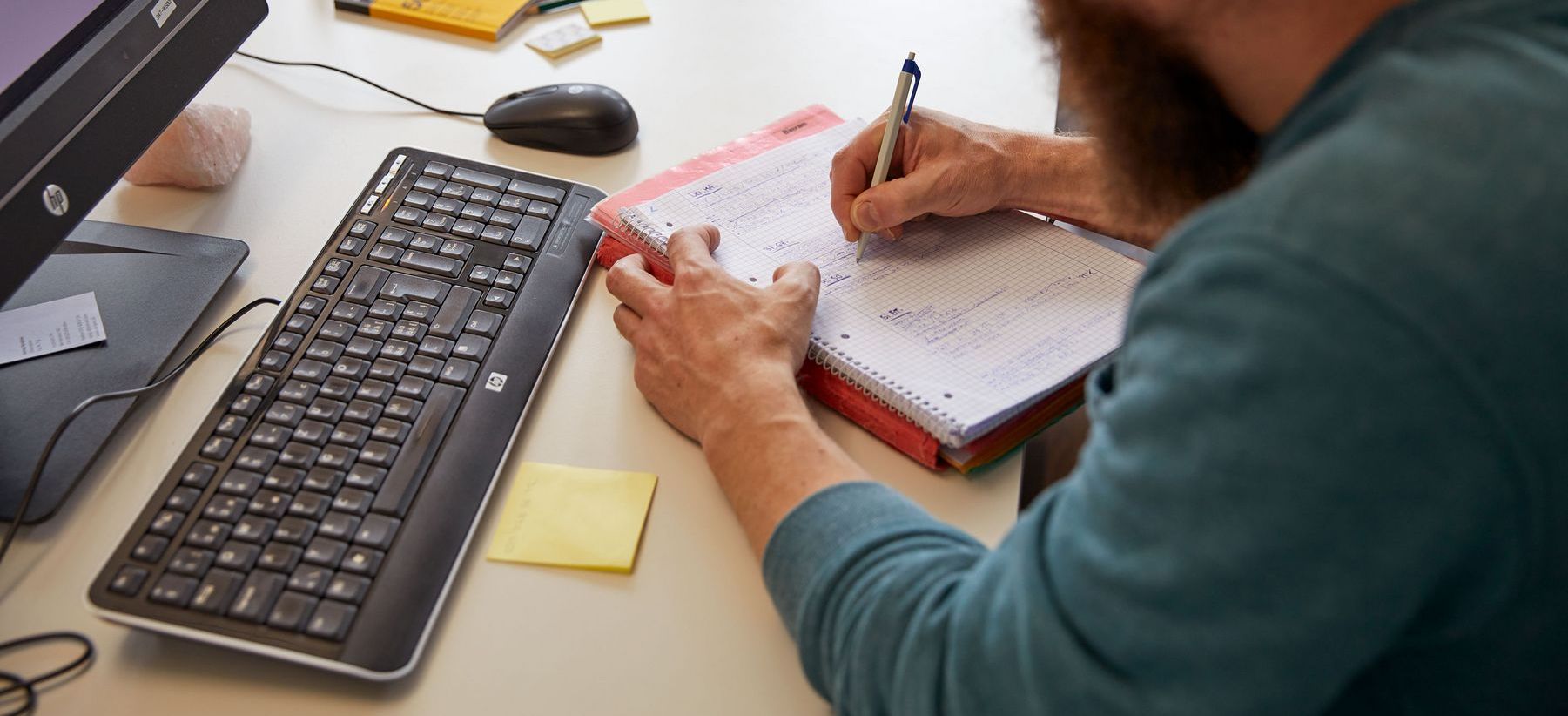 Eine Fachperson sitzt am Schreibtisch und notiert sich etwas
