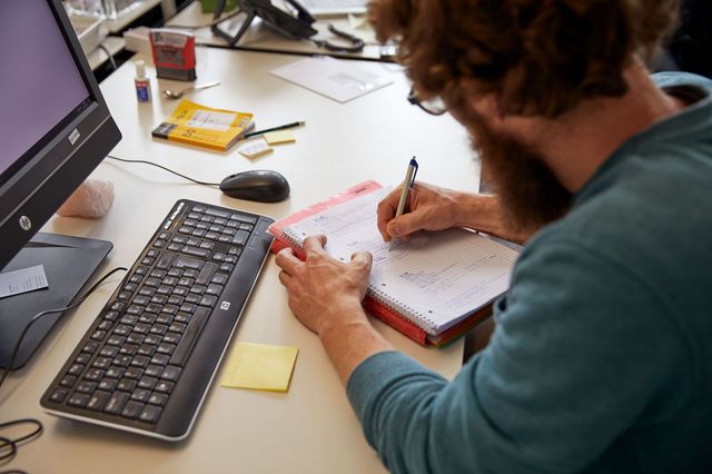 Eine Fachperson sitzt am Schreibtisch und notiert sich etwas