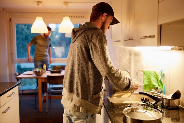 Ein Jugendlicher kocht in der Küche mit Wohnzimmer im Hintergrund