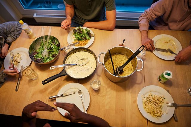 Eine Gruppe von Jugendlichen und Erwachsenen sitzt gemeinsam am Esstisch, auf dem Essen angerichtet ist