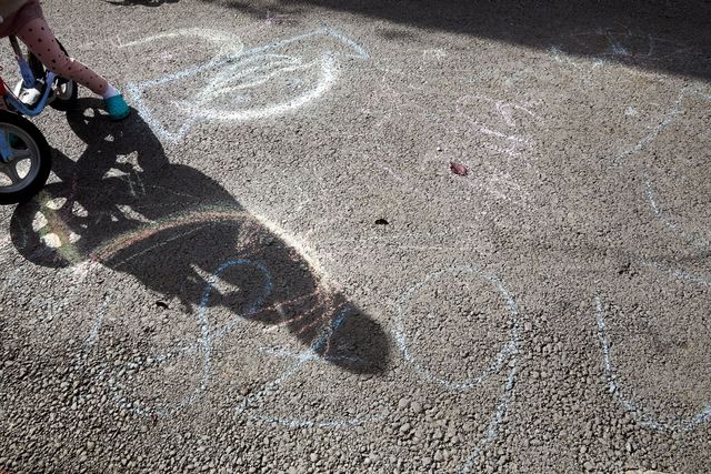 Kreidezeichnungen auf dem Straßenboden, daneben ein Fahrrad sowie die Schatten eines Kindes