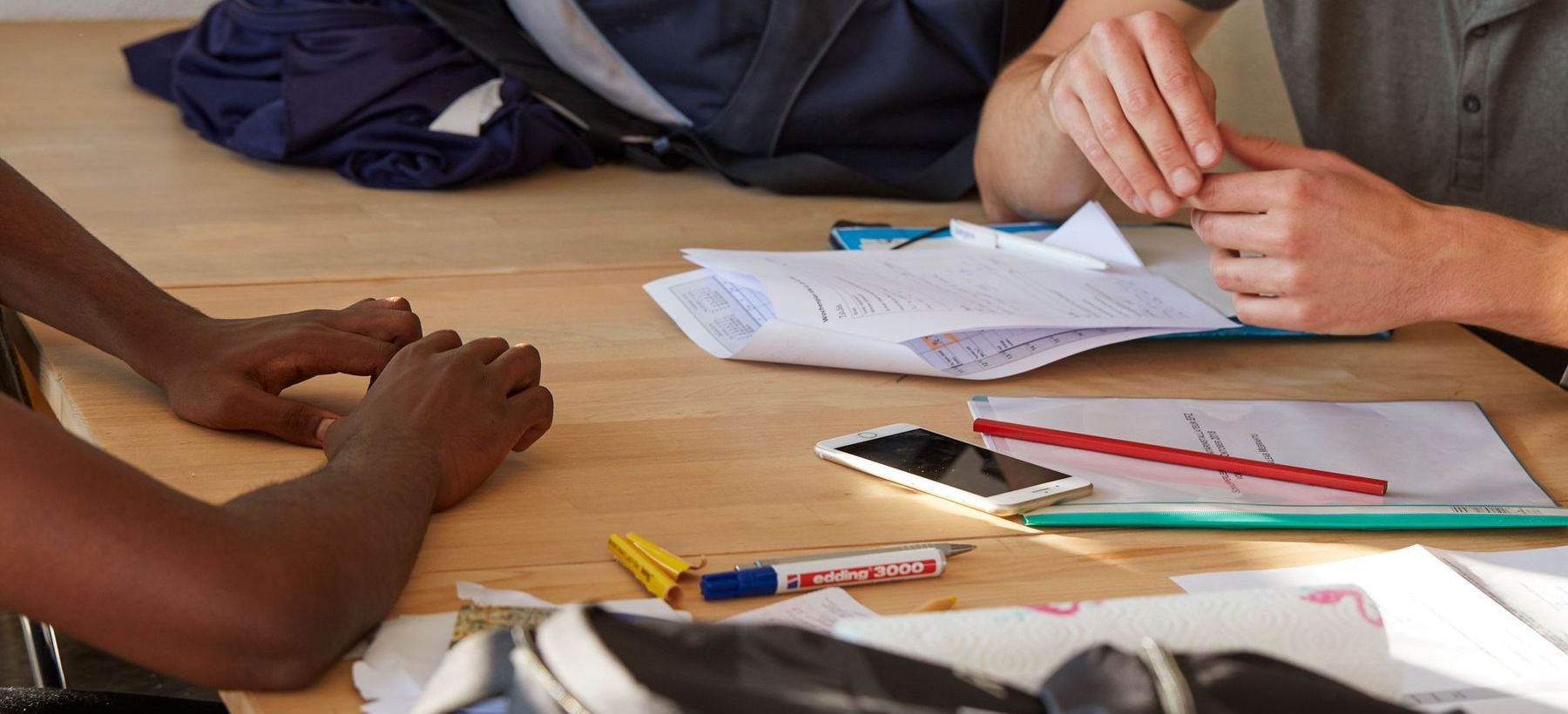 Eine Fachperson spricht mit einem Jugendlichen in einem Büro, während Schreibmaterialien und Blätter auf dem Tisch liegen