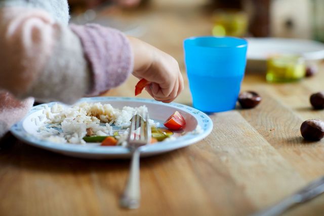 Eine Kinderhand greift nach Essen auf einem Teller