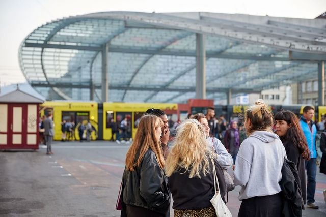 Jugendliche stehen in einer Gruppe auf dem Bahnhofsplatz und unterhalten sich